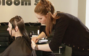 Bild aus dem Aktionsfilm: Die junge Friseurin schneidet mit krummen Rücken einer Kundin die Haare