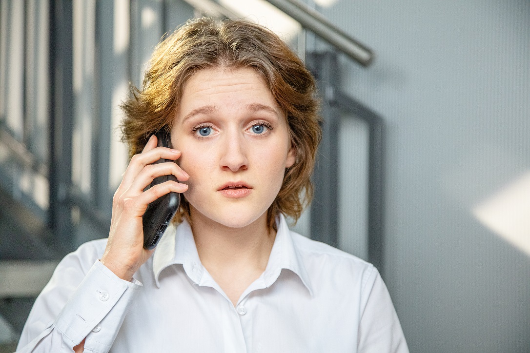 Alex, die junge Auszubildende hält ihr Handy ans Ohr um einen Notruf abzusetzen.