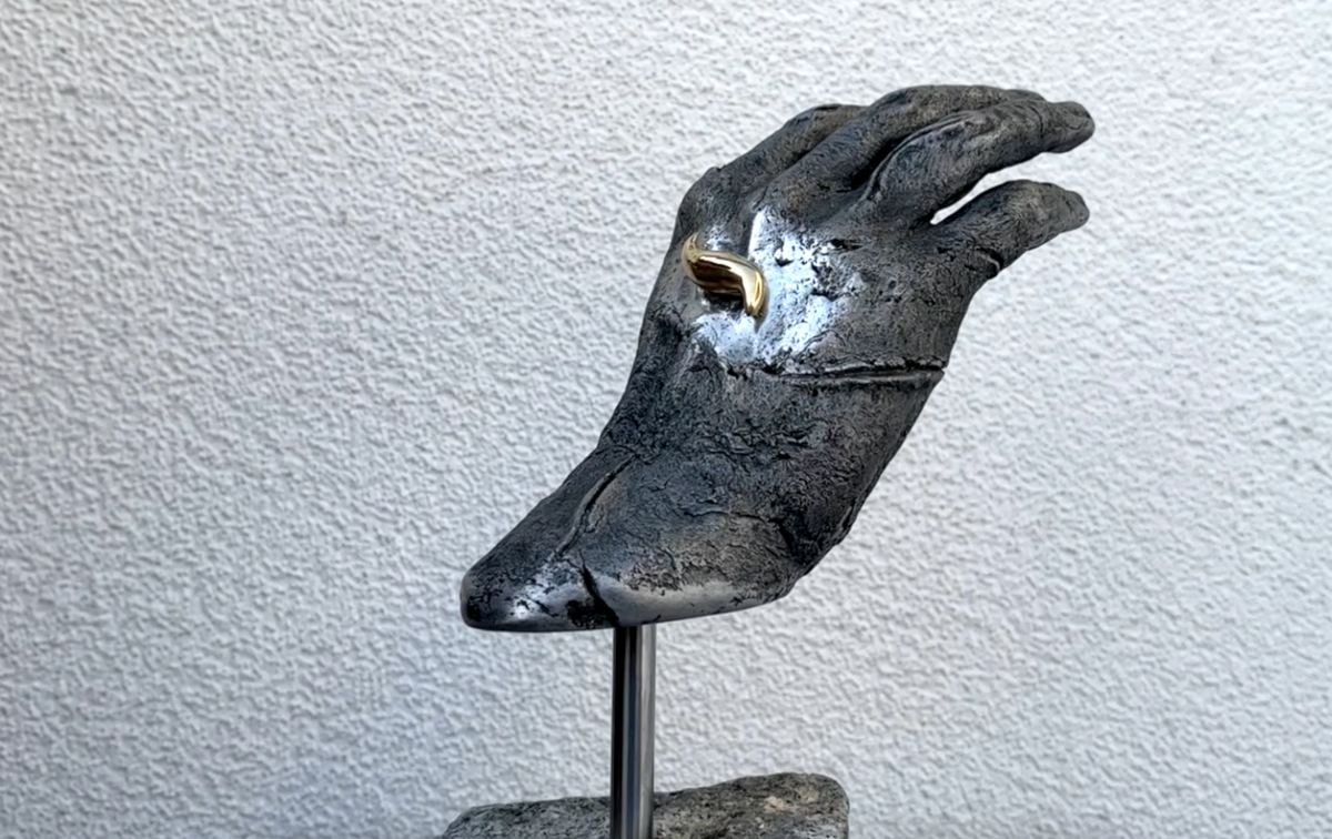 Skulptur einer Hand mit einem goldenen Cremeklecks